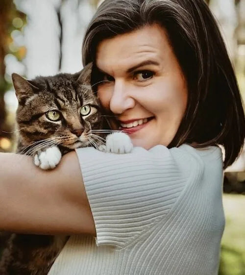 Woman holding a cat close to her face with a blurred natural background